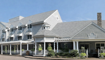 A large white hotel or inn with a wraparound porch, multiple gabled roofs, and a tidy front entrance along a street.