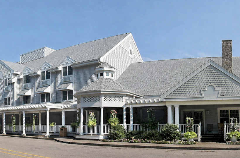 A large white hotel or inn with a wraparound porch, multiple gabled roofs, and a tidy front entrance along a street.