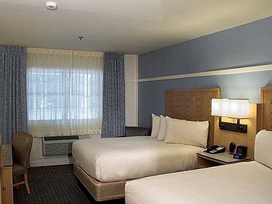 A hotel room with two large beds, nightstands, lamps, a desk and chair, and a large window with blue curtains.