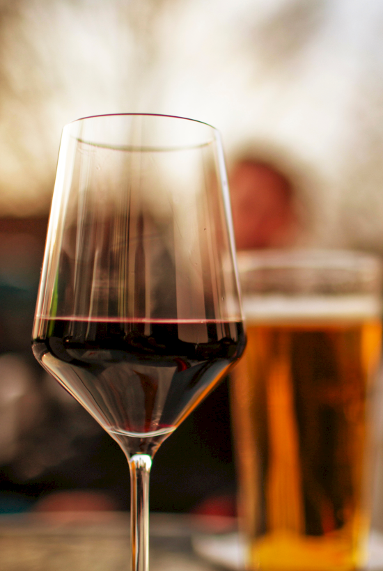 A wine glass with red wine in focus and a beer glass blurred in the background, indoors, warm lighting.