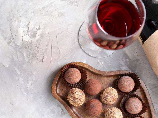 A wooden tray of assorted chocolate truffles, with a glass of red wine and a folded napkin on a light textured surface.